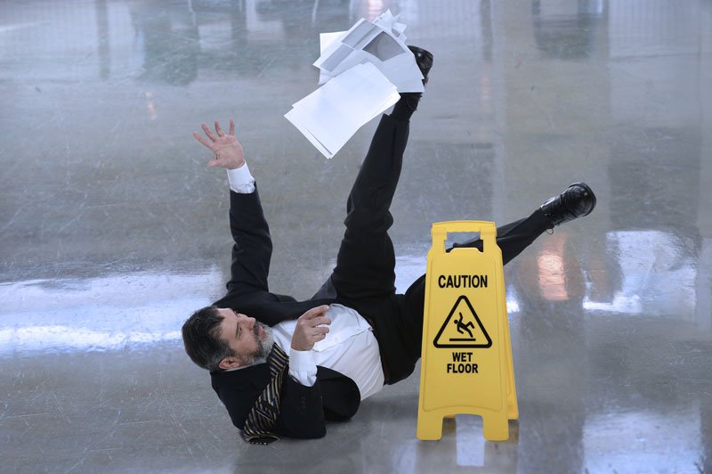 Photo d’un homme d’affaires glissant sur un plancher mouillé avec des documents entre les mains.