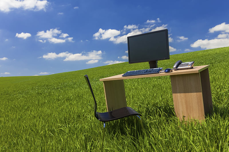 Office desk with a computer outside on an open green field