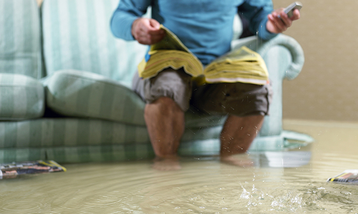 Photo d’un homme assis sur un divan dans une pièce inondée et tentant d’appeler pour obtenir de l’aide grâce à un bottin de téléphone trempé placé sur ses genoux.