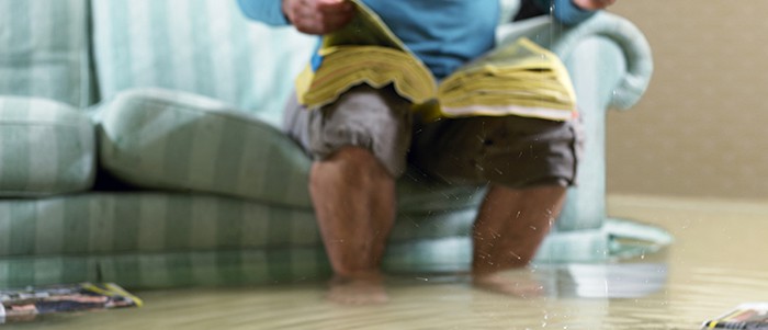 Man sitting on couch in flooded room attempting to call for help with a wet phonebook on lap