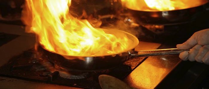 Photo d’un chef cuisinier faisant flamber de la nourriture dans une poêle sur une cuisinière au gaz.