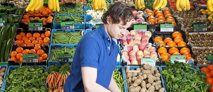 Photo d’un propriétaire d’épicerie plaçant des fruits et légumes à l’entrée du magasin.