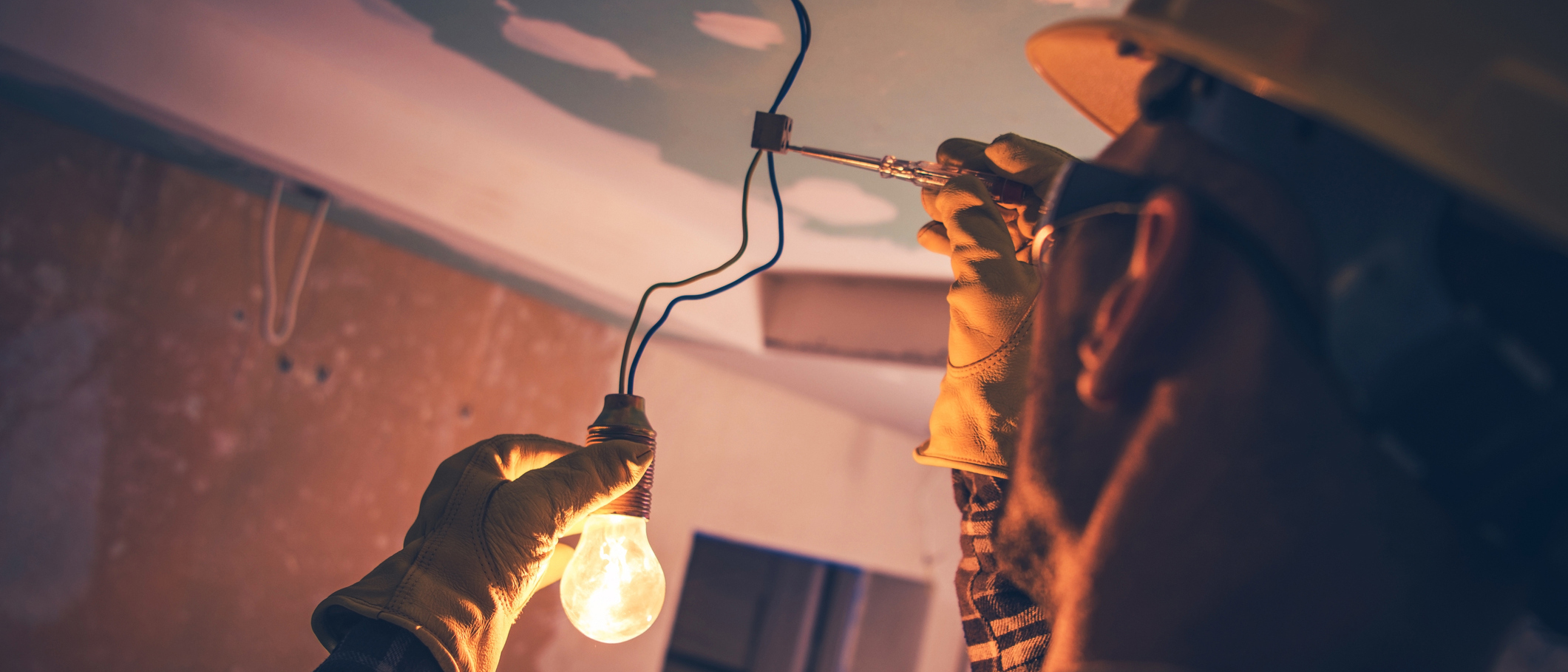 Photo d’un entrepreneur en électricité portant de l’équipement de protection et réparant les fils d’un luminaire.