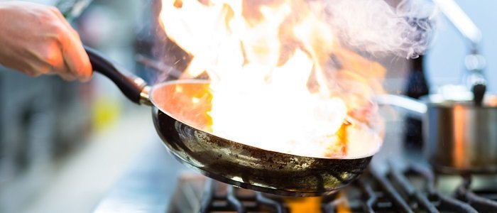 Photo d’un chef cuisinier faisant flamber de la nourriture dans une poêle sur une cuisinière au gaz.