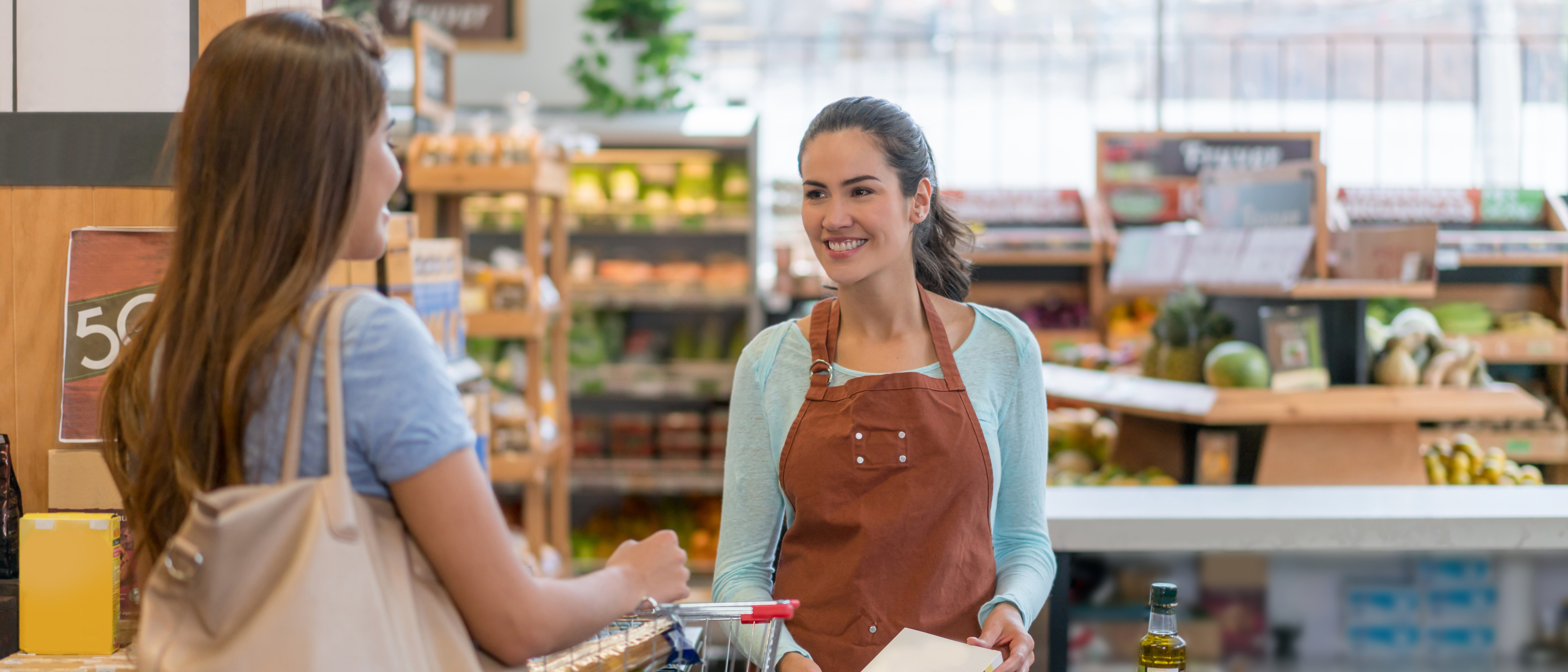 Photo d’une employée d’une épicerie accueillant une cliente et lui faisant payer ses achats.