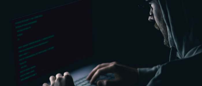 Hacker wearing a hood, sitting in front of a laptop breaking into the security system