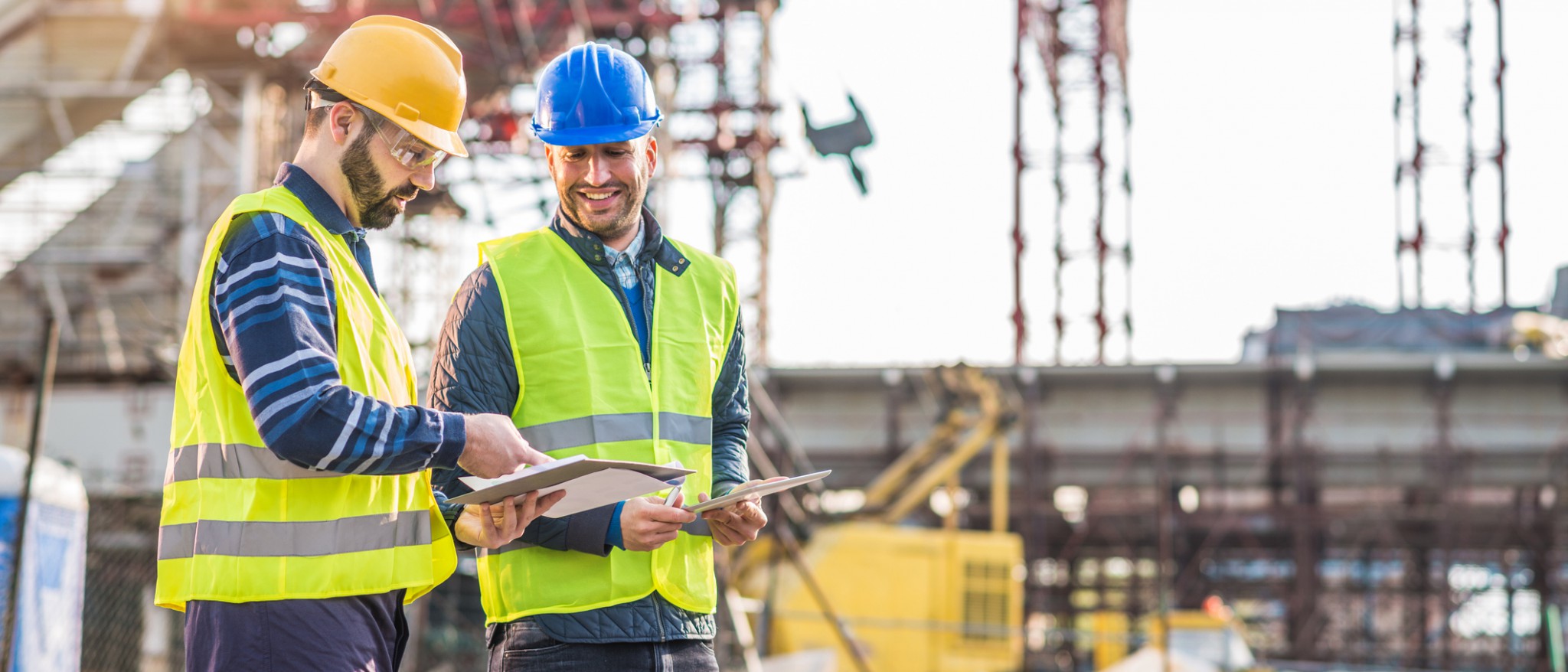 two construction workers wearing safety equipment conversing with each other