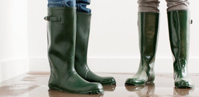 Photo rapprochée de deux personnes portant des bottes de pluie en caoutchouc vert.