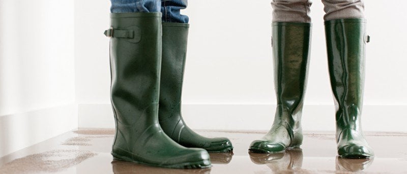 Photo rapprochée de deux personnes portant des bottes de pluie en caoutchouc vert.