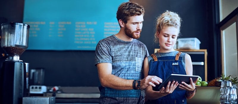 Male and female coffee shop owners looking at tablet 